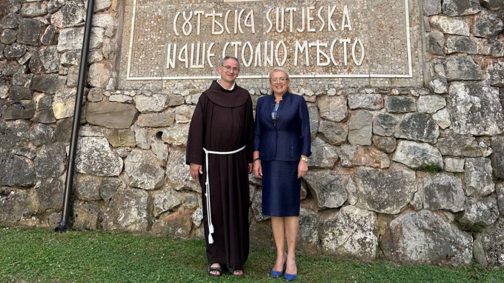 Lidija Bradara i franjevac ispred kamenog zida s natpisom Sutjeska, naše stolno mjesto