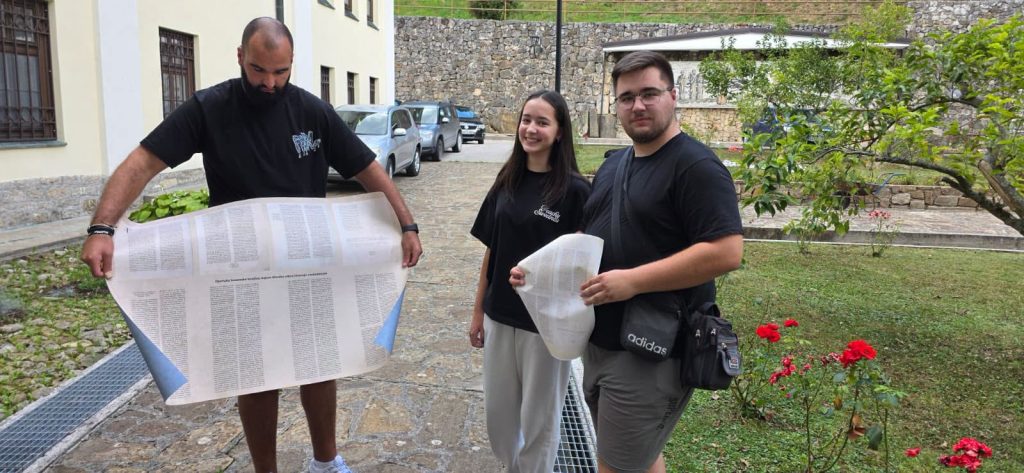 Tri osobe s velikim ispisima teksta u dvorištu samostana u Kraljevoj Sutjesci